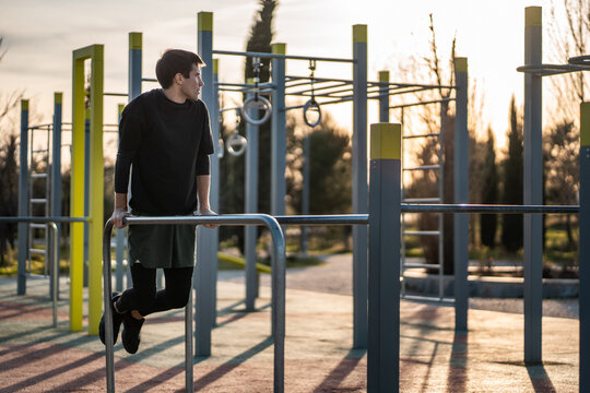young athletic man exercising fitness calisthenics workout and making dips at street gym during sunset for body improvement and strength training