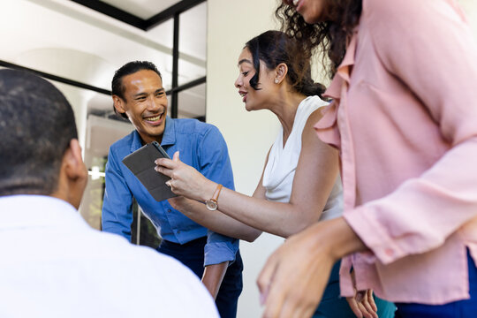 Diverse business team collaborating with tablet, sharing ideas and smiling at office
