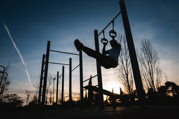 young athletic man exercising fitness calisthenics workout and making ring leg raises for abdomen...