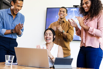 Diverse business team celebrating success with laptop in modern office