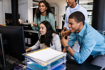 In office, diverse team collaborating around computer, focusing on project work