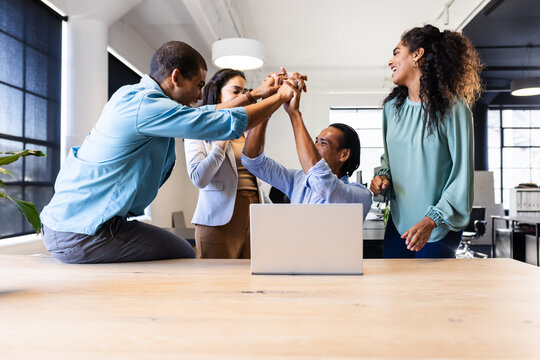 Diverse business team celebrating success around laptop in modern office