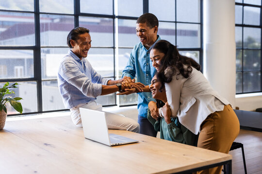 Diverse business team celebrating success around laptop in modern office