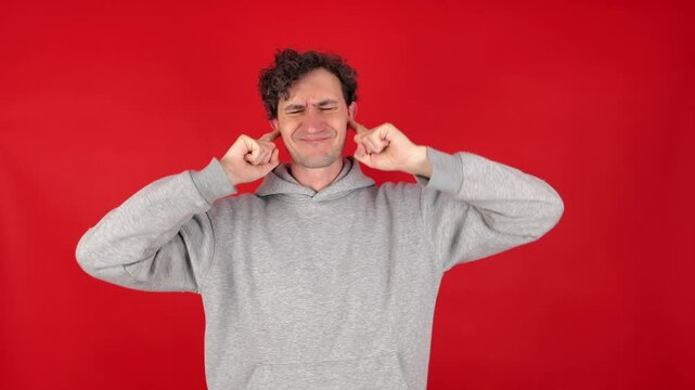 unhappy, angry, suffering curly man covers ears fingers, does not want listen screams, loud music, avoids stress. Isolated red background studio shot. concept - mental health, refusal hear information