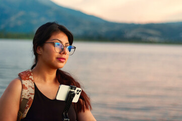 A Contemplative Young Woman Sitting by the Water with a Camera in Hand, Deep in Thought