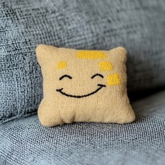 A small square cushion with a happy embroidered face design