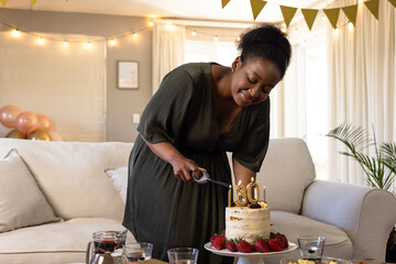 Woman cutting birthday cake with number 30 candles, smiling in living room, at home