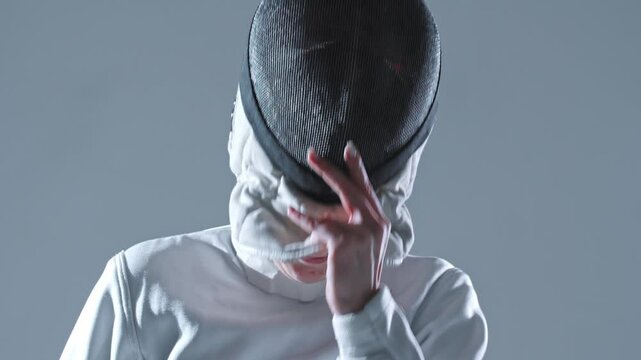 Fencing - young woman fencer in white suit takes off her helmet in white studio