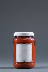 glass jar with red tomato or hot adjika pepper sauce with empty label mockup on isolated grey background, studio shot