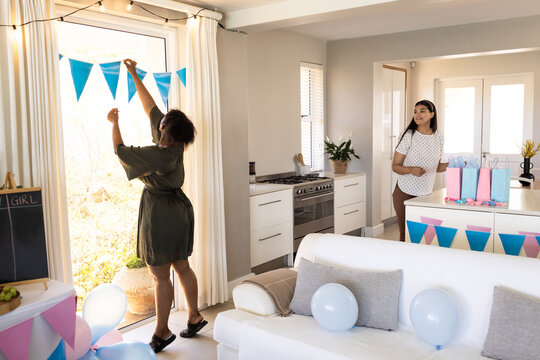 Decorating with blue bunting for celebration, diverse female friends preparing party, at home