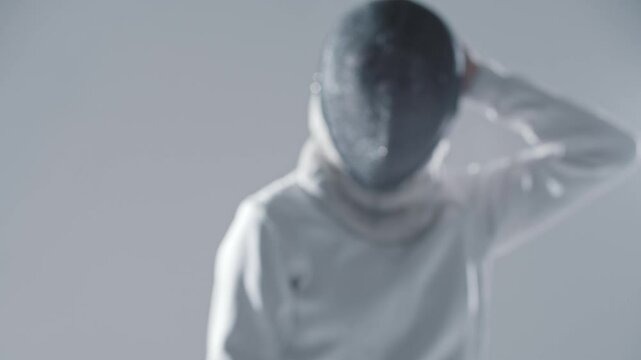 Fencing - young woman fencer in white suit puts on her protective helmet and aiming in the camera with a rapier