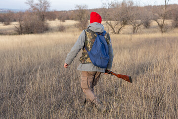 Mature hunter man holding a shotgun and walking through a field