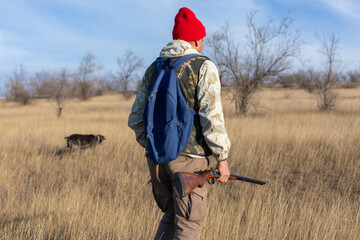 Mature hunter man holding a shotgun and walking through a field