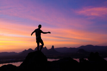Obraz premium silhouette of man standing on the hill at Phu Sub Lek in Lopburi, Thailand. Silhouette of positive man celebrating on mountain top with arms raised up.
