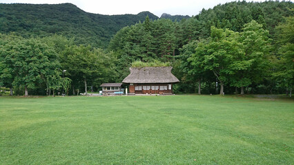 山やうっそうと茂る木々の中、中央に立つ茅葺き屋根の古民家風の建物