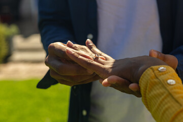 Man placing engagement ring on woman's finger in romantic outdoor setting