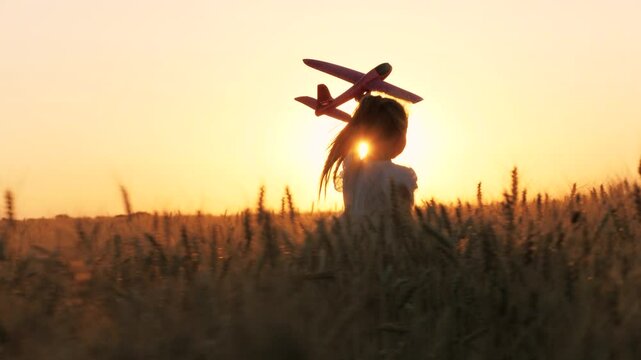 Cute little girl child running with plane toy playing at sunset sunrise wheat field happy childhood back view. Adorable female kid flying aircraft plaything pilot imagination fantasy enjoy freedom