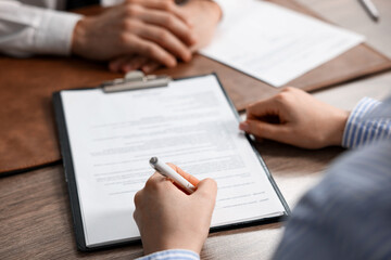 Client signing notarial document during meeting with lawyer at wooden table indoors, closeup