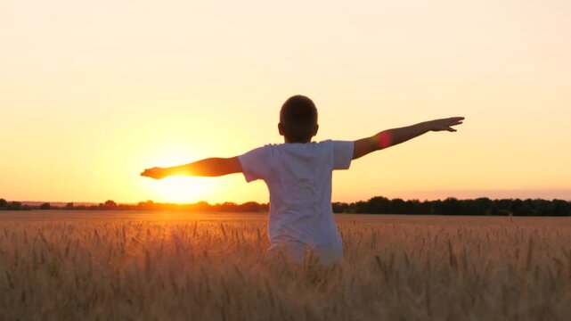 Happy male teen running on wheat field with open hands enjoy freedom at sunset sunrise back view closeup. Boy kid teenager relaxing imagine flying at dusk rye meadow sun sky forest horizon