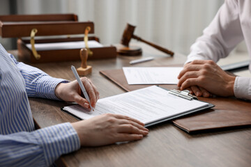 Client signing notarial document during meeting with lawyer at wooden table indoors, closeup
