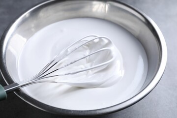 Whisk and whipped cream in bowl on grey table, closeup