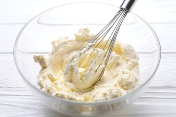 Bowl with whisk and whipped cream on white wooden table, closeup