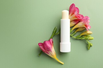 Lip balm and freesia flowers on light green background, flat lay. Space for text