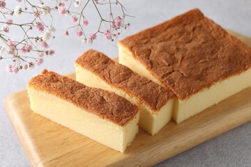 Tasty Japanese Castella sponge cake and flowers on light table, closeup