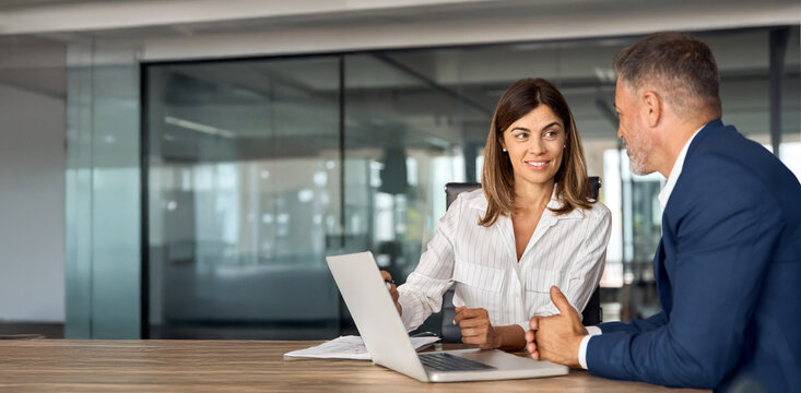 Mature team of partners sitting at table, business man and business woman discussing project on laptop in office. Two colleagues of professional business people working together. Copy space, banner