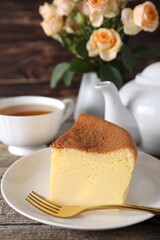 Tasty Japanese Castella sponge cake, tea, fork and flowers on wooden table, closeup