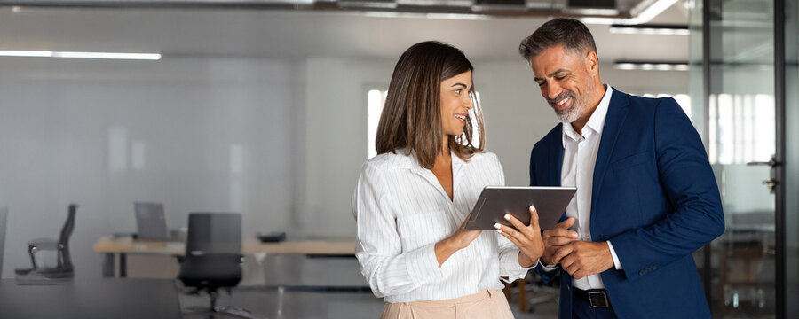 Mature businessman and businesswoman discussing project on tablet in office. Two partners woman, man colleagues professional businesspeople working together using digital gadget. Copy space, banner