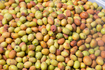 Jujube fruits, green and brown, fill a metal container. A mix of ripe and spoiled, their contrast tells a story of nature's cycle
