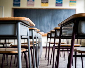 Close-up of empty school desks and chairs, light wood tops and metal legs, arranged in rows facing a blackboard, showcasing a classroom setting representing education and learning