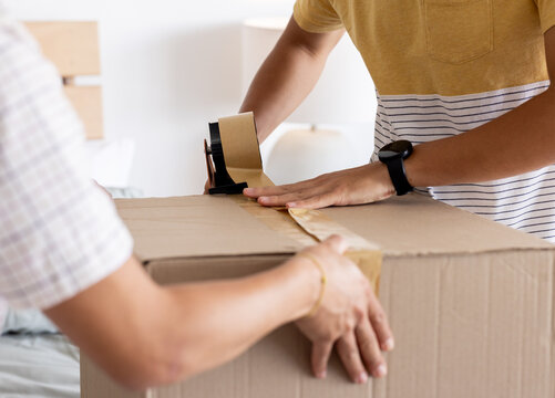 Father and son sealing cardboard box with tape at home, preparing for move