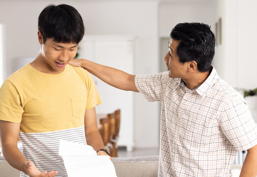 Father encouraging son while discussing school report at home, fostering support