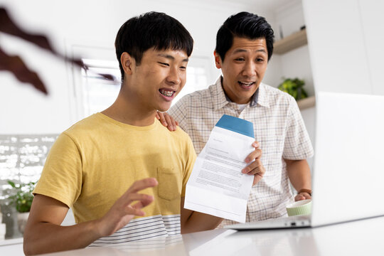 Asian father and son celebrating college acceptance letter together at home