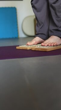 Bare feet stepping on wooden massage board, close-up view emphasizing reflexology therapy, balance practice in vertical video