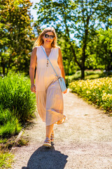 Summer in city. Beautiful happy middle-aged woman walking in city park on beautiful sunny day....