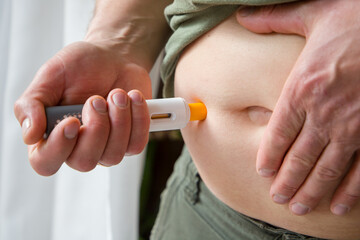 A man makes a self-injection into the abdomen using injection pen.