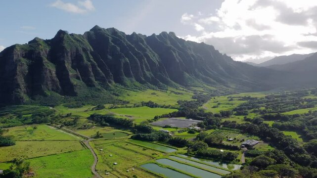 Kualoa Ranch Hawaii - majestic green mountains tower over lush valley with farms and ponds, capturing iconic tropical landscape and cinematic natural beauty