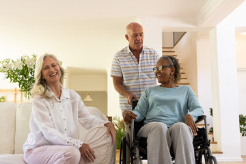 Senior diverse friends enjoying conversation at home, one woman in wheelchair smiling warmly