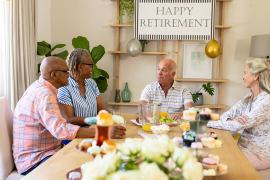 Senior diverse friends celebrating retirement with conversation and snacks at home gathering