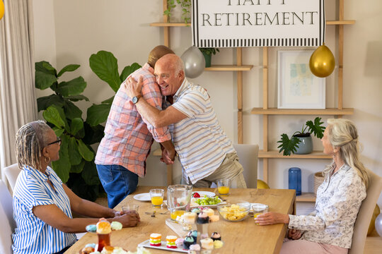 Senior diverse friends celebrating retirement with joyful hugs and delicious brunch at home