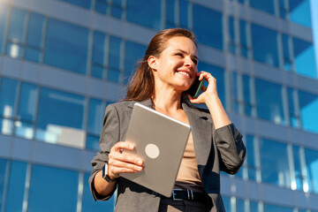 Businesswoman with digital tablet talking on mobile phone outdoors on city street