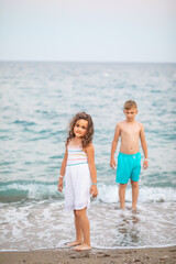 Cute little girl and teenager boy standing on the seashore at the beach near by sea or ocean in summer. Playful active kid. Holiday vacation with children.