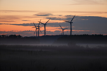 Wind turbines silhouetted against a colorful sunrise in a serene landscape