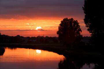 Obraz premium Colorful sunset reflecting on a serene river surrounded by trees and hills