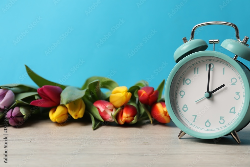 Poster spring time. alarm clock and beautiful tulips on wooden table against light blue background