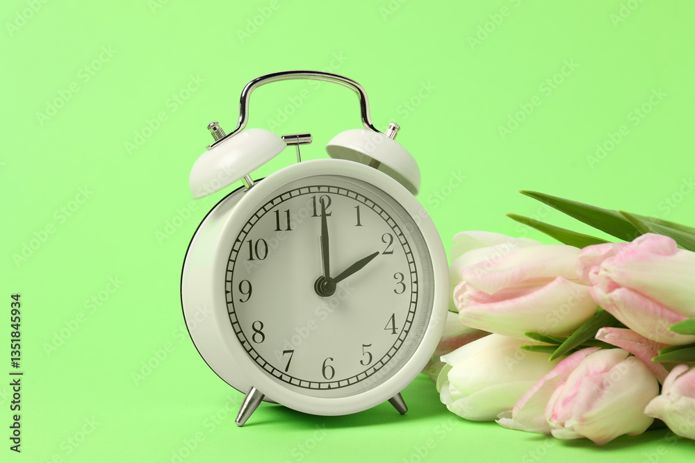 Poster spring time. alarm clock and beautiful tulips on green background