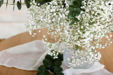 Bouquet of beautiful gypsophila flowers and eucalyptus branches in vase on table indoors, closeup